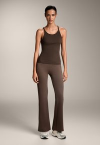 Rjava rebrasta majica brez rokavov v kombinaciji z razširjenimi rjavimi legicami, narejenimi iz gladkega materiala, s prilegajočim se krojem in preprostim, diskretnim dizajnom.