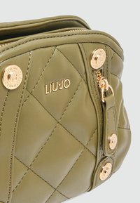 Groene gequiltte handtas van faux leather met goudkleurige hardware, voorzien van een logo, ritssluiting en decoratieve knopen aan de zijkant.