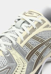 Letvægts sportssko i grå og creme mesh med teksturerede paneler, brune accenter og snøresystem for en sikker pasform.