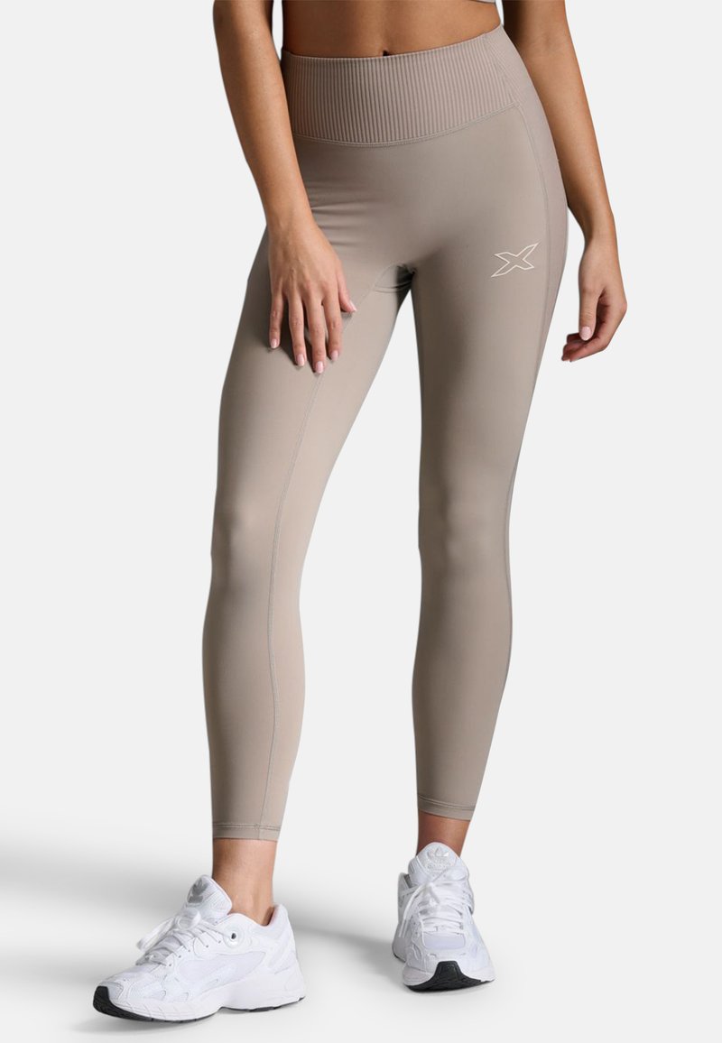 Beige High-Waist-Leggings mit geripptem Bund, glatter Textur und subtilen Nähten. Dazu weiße Sportschuhe.