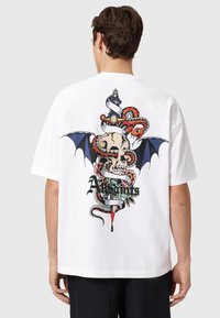 Λευκό βαμβακερό t-shirt με μεγάλο πολύχρωμο σχέδιο στην πλάτη, που απεικονίζει ένα κρανίο, φίδια και φτερά νυχτερίδας με ανθισμένες λεπτομέρειες.