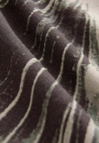 Gros plan sur un tissu doux avec des rayures ondulées et irrégulières blanches et grises sur un fond brun foncé.