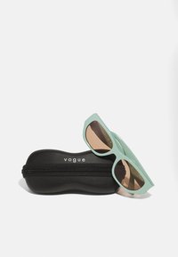 Ochelari de soare verzi cu ramă geometrică și lentile maro, așezați pe un toc tare negru, dotat cu fermoar și logo-ul "vogue".