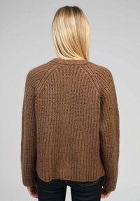 Pull en laine brun avec une texture côtelée, doté de manches longues et d'un col rond. L'ourlet est légèrement court à l'arrière.