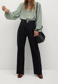 Jasnooliwona bluzka z długim rękawem ozdobiona guzikami, w zestawieniu z czarnymi dżinsami o wysokim stanie i szerokich nogawkach. Brązowe buty na obcasie i czarna torba.