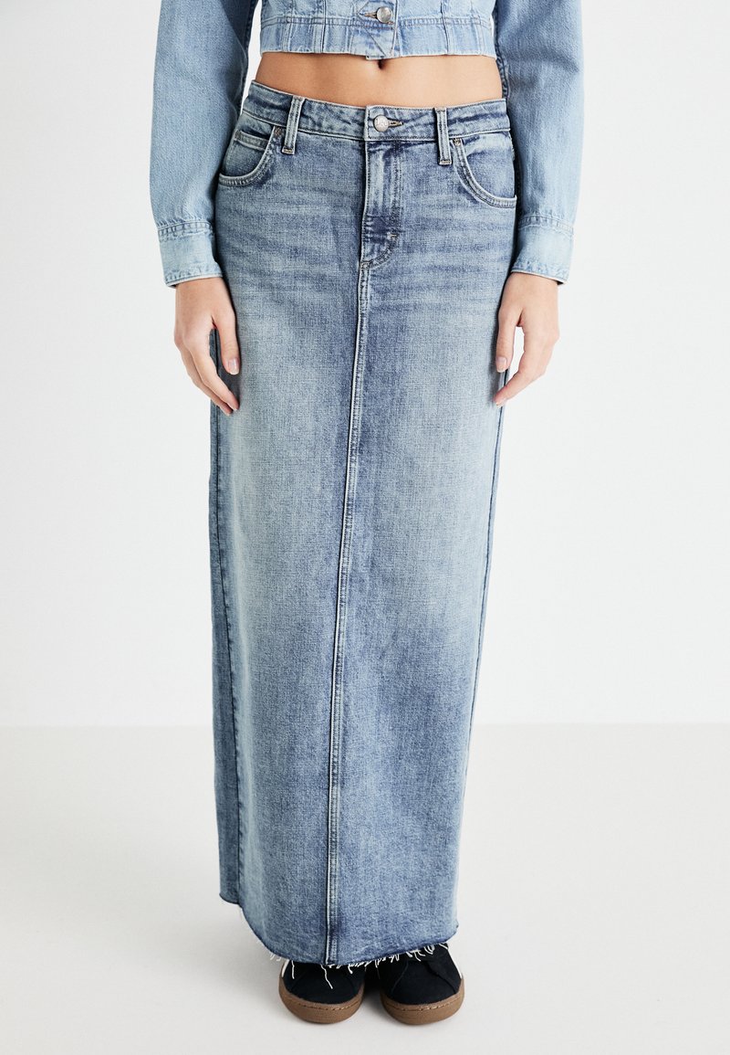 Gonna lunga in denim di colore azzurro con taglio dritto, cuciture frontali e orlo sfrangiato; abbinata a scarpe scure.