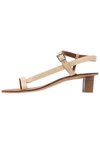 Beige lädersandal med tunna remmar och en liten, texturerad träklack. Platt sula med minimal detaljering och en justerbar spänne.