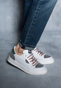 Sneakers bianchi in pelle con dettagli in suede grigio e tallone verde. Lacci marroni, dettaglio laterale perforato e suola in gomma testurizzata.