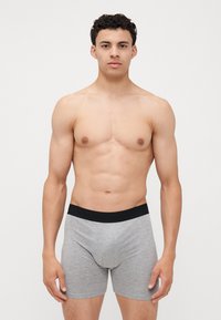 Graue Baumwollboxershorts mit einem schwarzen elastischen Bund, ausgestattet mit einem enganliegenden Design und glatter Textur, präsentiert von einer männlichen Figur.