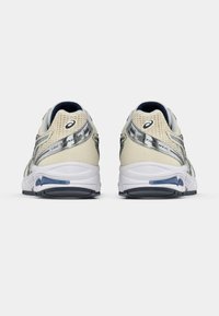 Buty do biegania w kolorze kremowym i srebrnym, z cholewką z siateczki i białą, amortyzowaną podeszwą. Posiadają niebieskie akcenty oraz logo na pięcie.