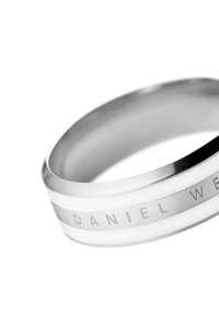 Hienosti muotoiltu hopeakäsikoru, jossa on valkoisia yksityiskohtia, ja jonka pinnassa on kaiverrettuna "DANIEL WELLINGTON". Sivustaltaan sileä, pyöreä muoto.