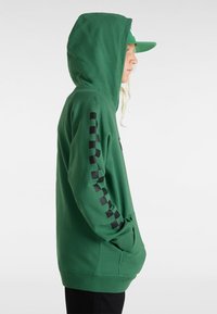 Sudadera verde con un bolsillo frontal, que presenta rayas de ajedrez negras a lo largo de la manga izquierda y una capucha con cordón.