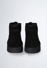 Stivali alla caviglia in suede nero con un morbido rivestimento interno, punta rotonda e suola in gomma nera spessa. Presentano dettagli in cucitura lungo i lati.