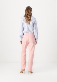 Vaqueros rosas de tiro alto y pierna recta con bolsillos traseros, combinados con una camisa de manga larga a rayas en azul claro y blanco.