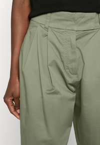Spodnie w wysokim stanie z krokami w miękkiej oliwkowej bawełnie. Charakteryzują się dopasowanym pasem oraz bocznymi kieszeniami, a także gładkim, teksturowanym wyko�ńczeniem.