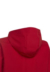 Veste à capuche rouge avec une texture lisse et mate, dotée d'une capuche arrondie et de coutures minimales, conçue pour la fonctionnalité et le confort.