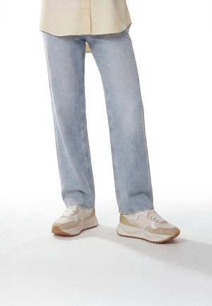Lyseblå jeans med lige ben båret med beige og hvide chunky sneakers på hvid baggrund.