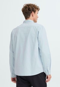 Lichtblauw langemouwen shirt van zachte stof, met een button-down kraag, knoopmanchetten en een afgeronde zoom. Achteraanzicht weergegeven.