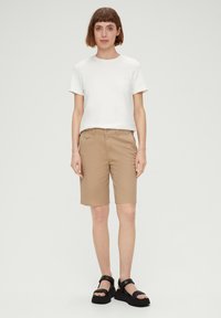 Witte T-shirt met korte mouwen, beige shorts en zwarte platform sandalen. De shorts hebben zakken en het shirt heeft een ronde hals.