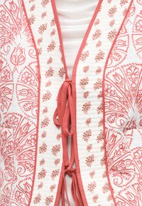 Λευκό ύφασμα με κοραλλί λουλουδένια και παϊέτα σχέδια, με κοραλλί περιθώριο και κλεισίματα με κορδόνια στο κέντρο μπροστά.