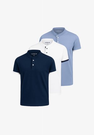 Weißes Polohemd mit marineblauem Kragen und Manschetten, taillierte Passform, kombiniert mit dunklen Jeans und weißen Sneakern. Model steht vor einem neutralen Hintergrund.