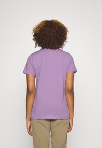 Camisa polo de manga corta morada con dobladillo recto y textura suave, vista desde la parte de atrás. Combinada con pantalones cargo marrón claro.