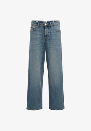 Έφηβος αγόρι με μπλε σκουφί, γαλάζιο πουκάμισο με κουμπιά, φαρδιά τζιν και μπεζ παπούτσια, στέκεται και κοιτάζει προς τα δεξιά.