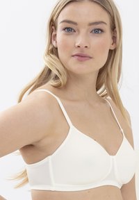 Soutien-gorge en tissu doux beige clair avec des bretelles fines réglables et un design de cups triangulaires. Construction sans coutures et détails de texture subtils.