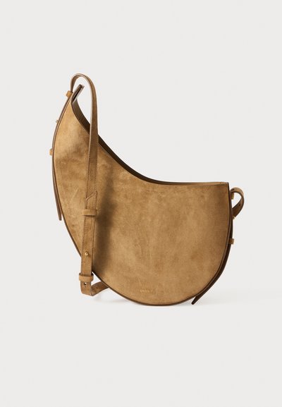 Suede braune Tasche mit asymmetrischem Design, verstellbarem Riemen und glatter Textur. Verfügt über goldfarbene Beschläge und eine minimalistische Markenpräsenz.