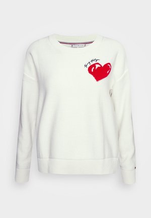 Suéter blanco de punto con cuello redondo, que presenta un diseño de corazón rojo y costuras negras con el nombre de la marca "Tommy Hilfiger" encima del corazón.