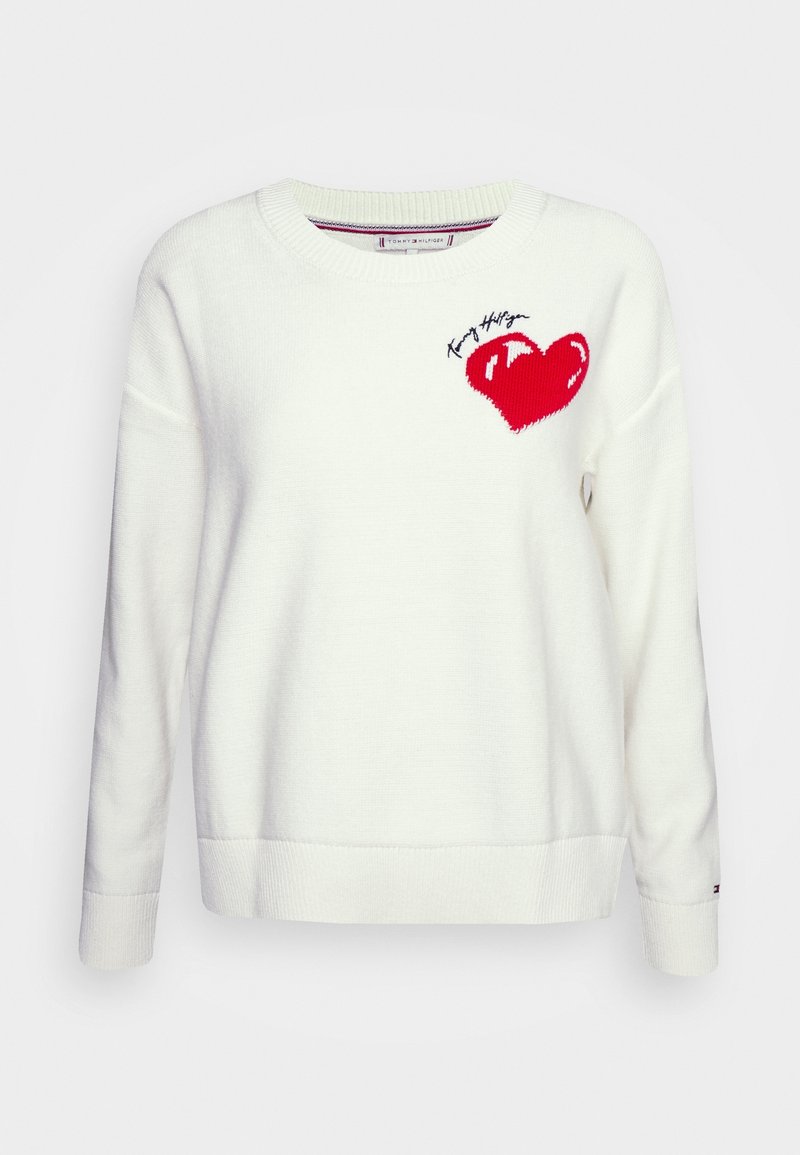 Biały dzianinowy sweter z okrągłym dekoltem, z czerwonym sercem i czarnym przeszyciem, z nazwą marki "Tommy Hilfiger" nad sercem.