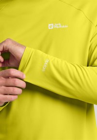 Maglietta a manica lunga verde lime con cuciture piatte. Presenta il logo Jack Wolfskin e il testo "Texdri" sulla manica. Tessuto morbido e elastico.