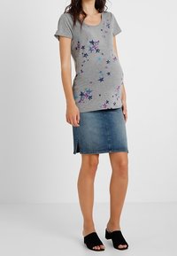 Camiseta de maternidad gris de manga corta con estampado de estrellas multicolores, combinado con una falda de mezclilla con una ligera abertura y zapatos negros sin cordones.