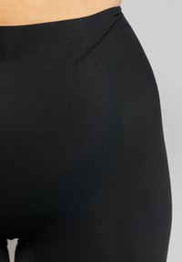 Leggings neri a vita alta realizzati in un tessuto liscio ed elasticizzato; presentano una vita senza cuciture e un design aderente e affusolato.