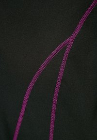 Mustaa kangasta, jossa on näkyvät violetit ommelviivat, ja joka esittää teksturoitua ulkonäköä sekä erottuvia kaarevia saumoja.
