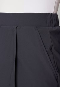 Black pleated skirt featuring an elastic waistband and smooth, textured fabric, with side pockets and neat stitching details.