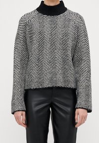 Hřejivý pletený svetr s černým stojáčkem, zdobený šedobílým herringbone vzorem. Hladké manžety a spodní lem, jemně texturovaný.