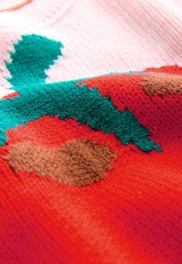 Tissu tricoté avec un motif abstrait rouge, vert et marron montrant des mailles de fil texturées en gros plan.