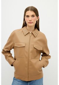 Brun faux læderjakke med lynlås foran, to brystlommer og detaljer med nitter på kraven. Har en afslappet pasform og en glat tekstur.