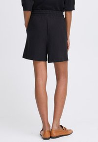 Shorts noirs légers avec une taille élastique, des poches latérales et une coupe décontractée, arrivant à mi-cuisse. Texture lisse, design simple.