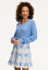 Hemelsblauw gebreid sweater met een v-hals en een gegolfd patroon, gecombineerd met een witte rok met blauwe palmboomborduring en rimpeldetails.