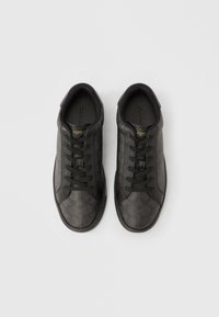 Μαύρο αθλητικό παπούτσι με υφή από δέρμα στο πάνω μέρος, που διαθέτει διακριτικό μοτίβο λογότυπου, στρογγυλή μύτη και μαύρα επίπεδα κορδόνια, τοποθετημένο σε λευκό φόντο.