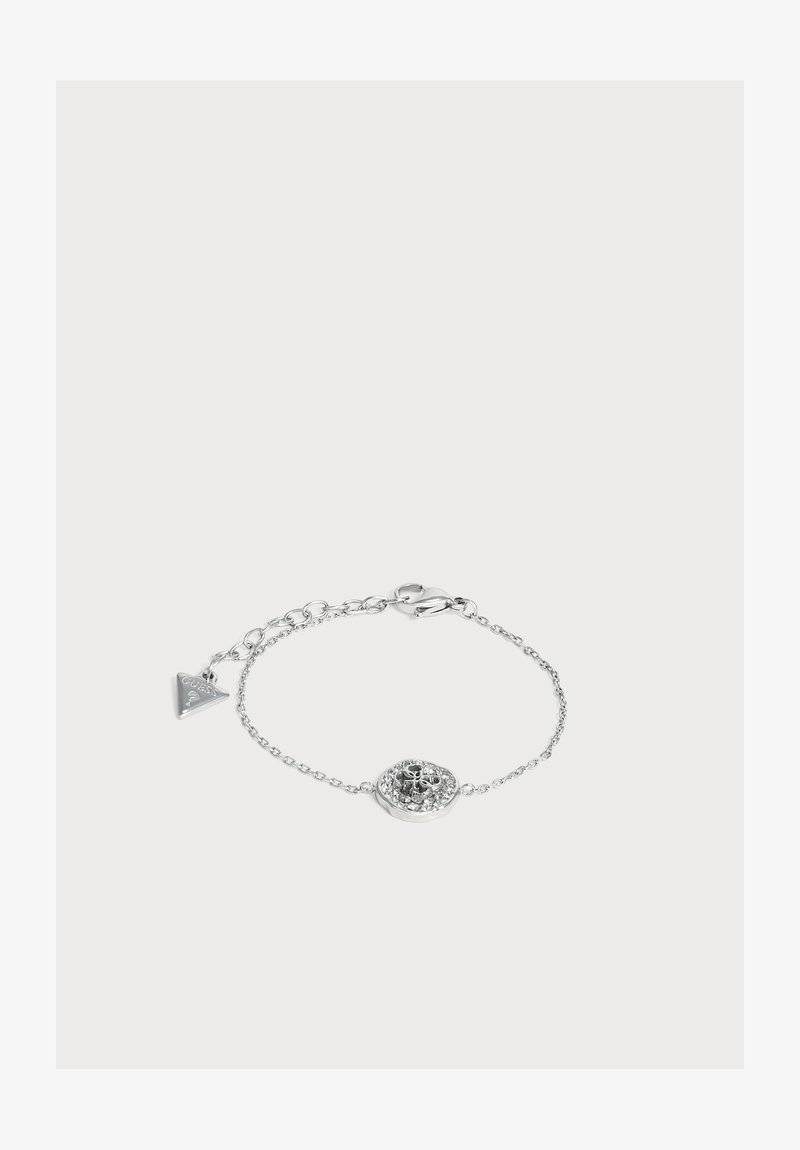 Bracelet chaîne en argent délicat avec un pendentif floral rond au centre et une petite étiquette triangulaire de marque près du fermoir.