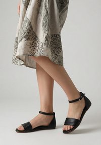 Benenden met zwarte enkellaarzen met riempje, gecombineerd met een beige rok met abstracte zwarte patronen.