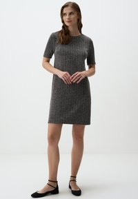 Abito grigio a maglia con maniche corte, scollo rotondo e motivo testurizzato. Abbinato a ballerine nere con cinturini incrociati alla caviglia.