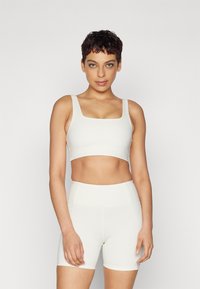 Conjunto de roupa ativa branco composto por um top cropped de decote quadrado e calções de cintura alta. Textura suave, costuras mínimas e um design ajustado.