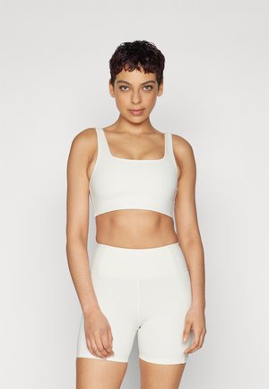 White activewear set featuring a square-neck crop top and high-waisted shorts. Smooth texture, minimal seams, and a fitted design.
