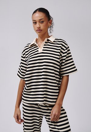 Polo à manches courtes rayé en noir et crème, avec une texture douce et un col en V. Associé à un pantalon rayé assorti.