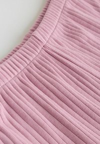 Približek roza rebraste tkanine z elastičnim pasom, ki prikazuje teksturo in podrobnosti šivov.