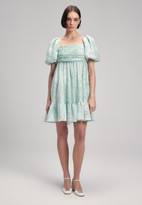 Vaaleansininen mekko, jossa on puffihihat, neliökaula-aukko ja rypistynyt vartalo. Teksturoitu kukkakuosi, kellottava helma ja kerroksellinen röyhelödetail.